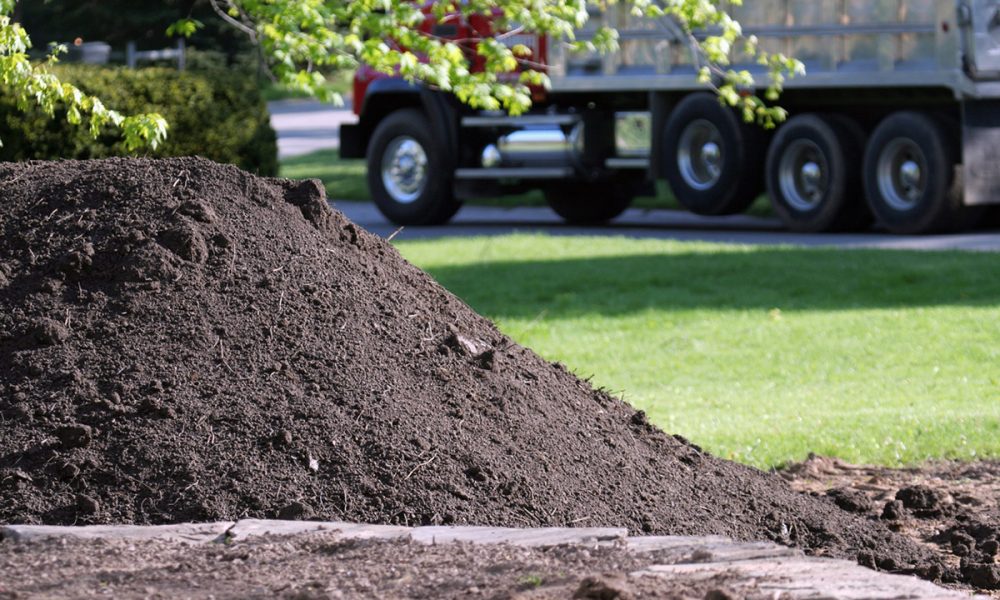 Large Dump Truck leaves residential property after delivering pile of topsoil - foreground focus with deliberate background blur.
